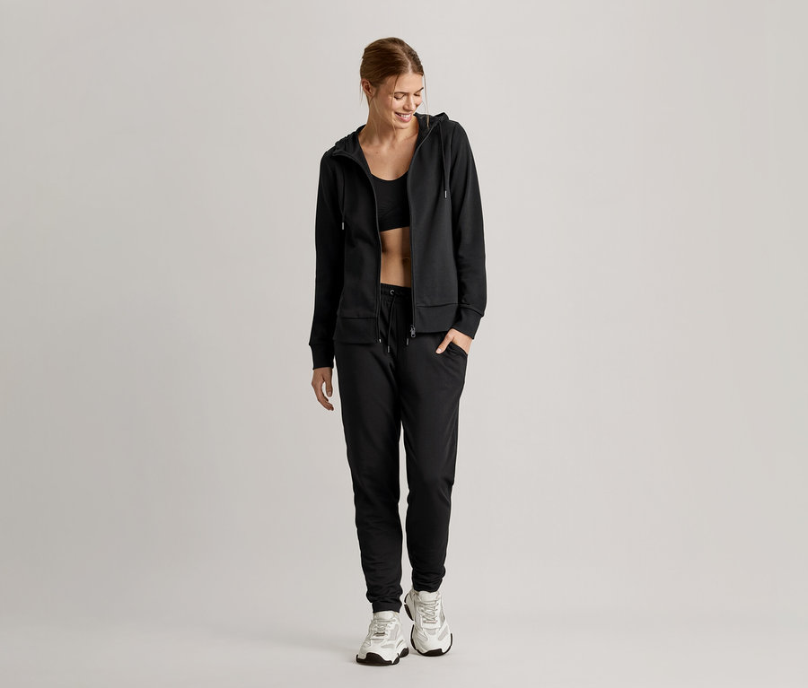 Femme portant un pantalon de survêtement noir et un soutien-gorge de sport Seamless noir avec une veste de survêtement ouverte par-dessus.