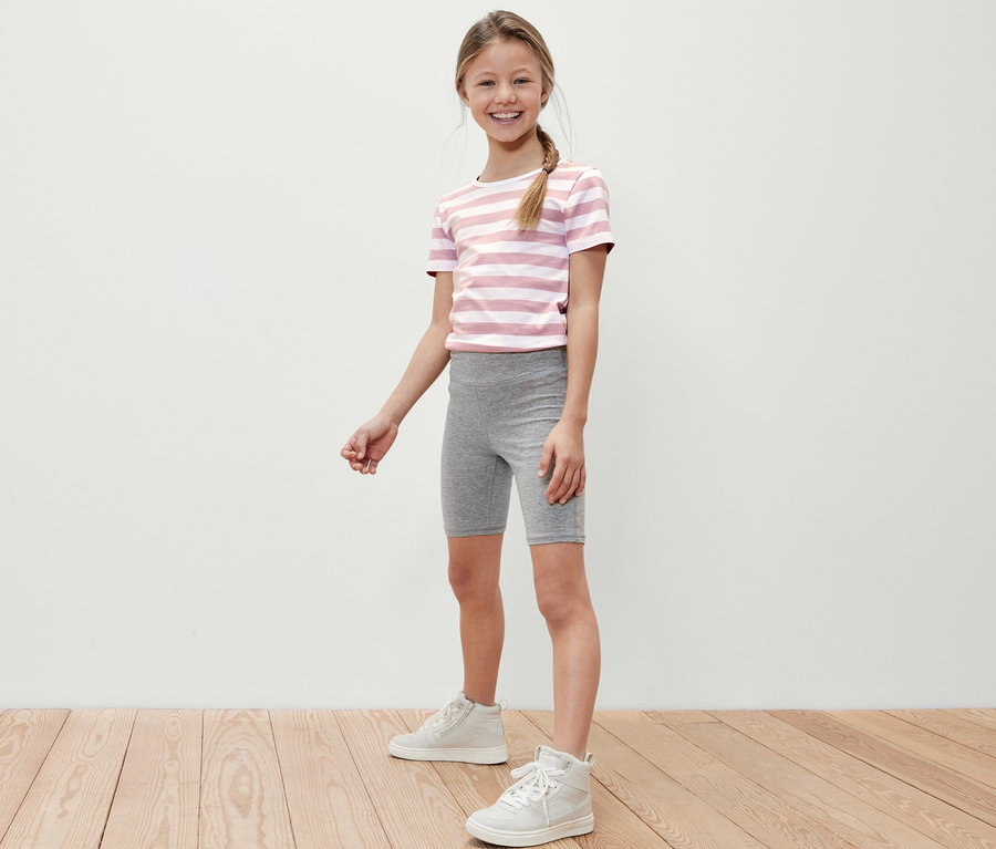 Une fille souriante pose, portant des leggings de cycliste gris et un t-shirt rayé.