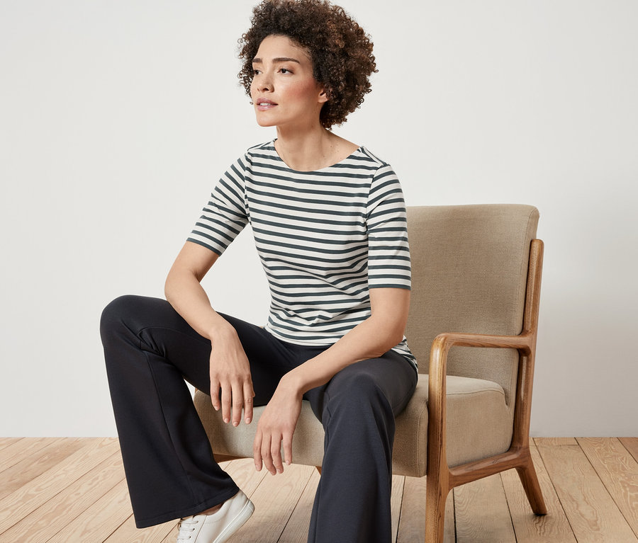 Une femme est assise sur une chaise et porte un t-shirt à demi-manches vert rayé.