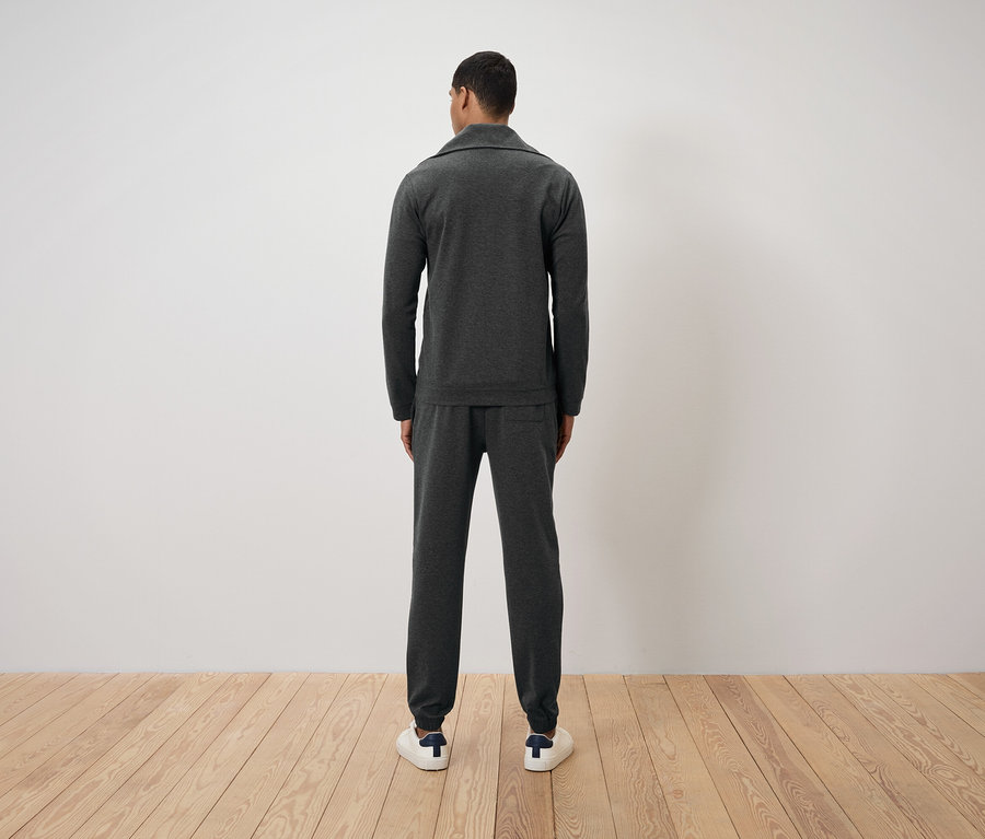 Un homme, vu de dos, porte un survêtement gris foncé et des baskets blanches.