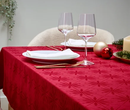 Une table dressée avec une nappe rouge, des assiettes blanches, des verres à vin, des couverts dorés, des décorations et une bougie.