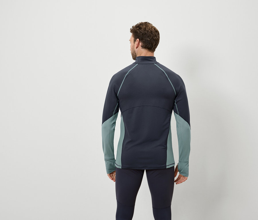 Un homme, vu de dos, porte un haut à manches longues bleu foncé avec des empiècements bleu-vert et un legging bleu foncé.