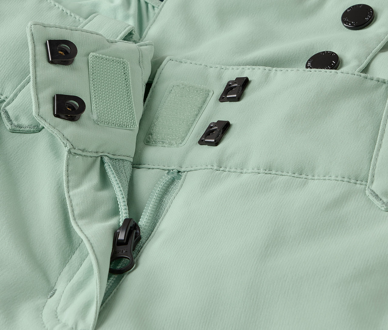 Gros plan d'un pantalon vert clair avec fermeture éclair et bouton.