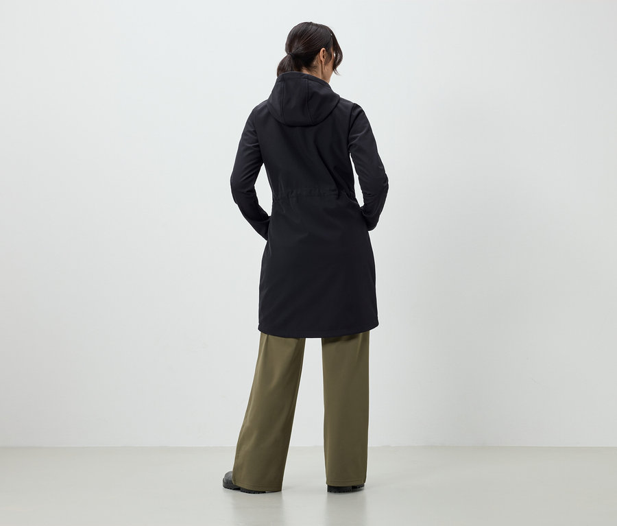 Une femme, dos à la caméra, porte un manteau noir et un pantalon vert.