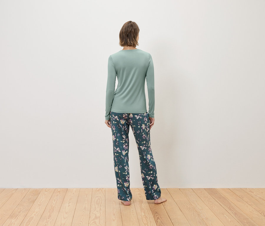 Vue de dos d'une femme portant un t-shirt à manches longues vert menthe et un pantalon à fleurs vert foncé.