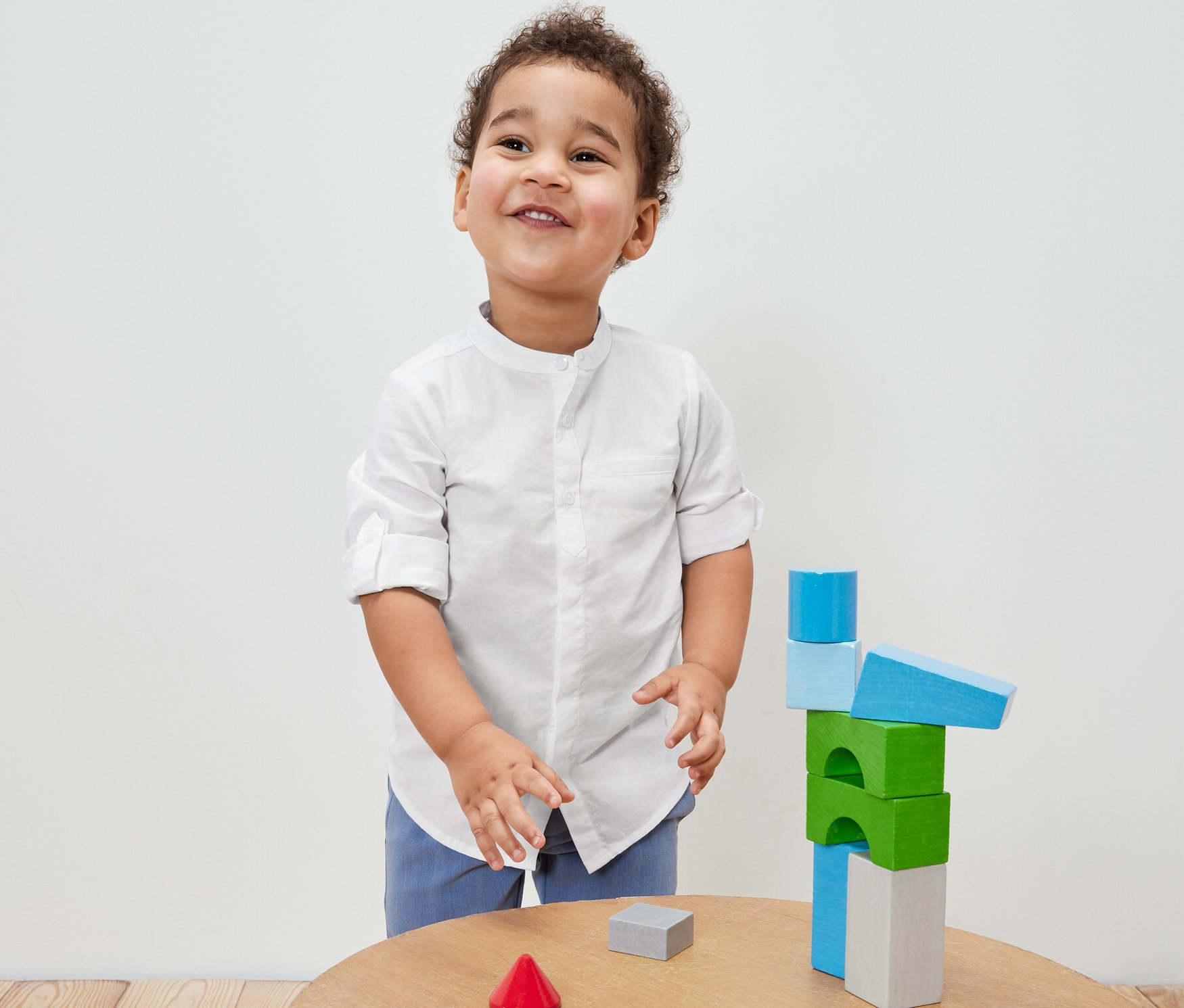 Un garçon en chemise pour enfant joue avec des blocs de construction en bois colorés sur une table.