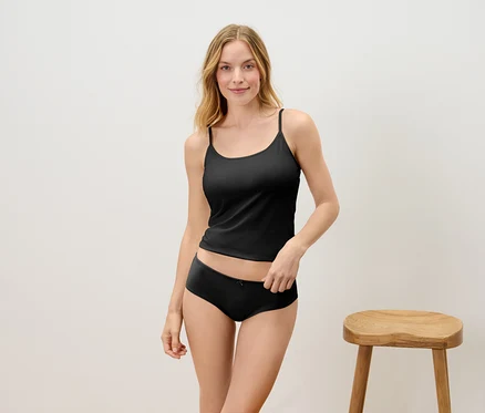 Une femme blonde pose en haut et culotte noirs devant un tabouret en bois.