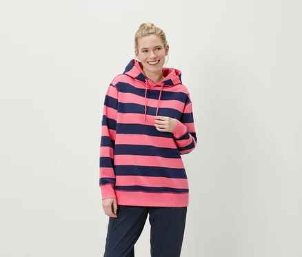 Femme blonde souriante portant un sweat à capuche rayé rose et bleu marine et un pantalon bleu marine.