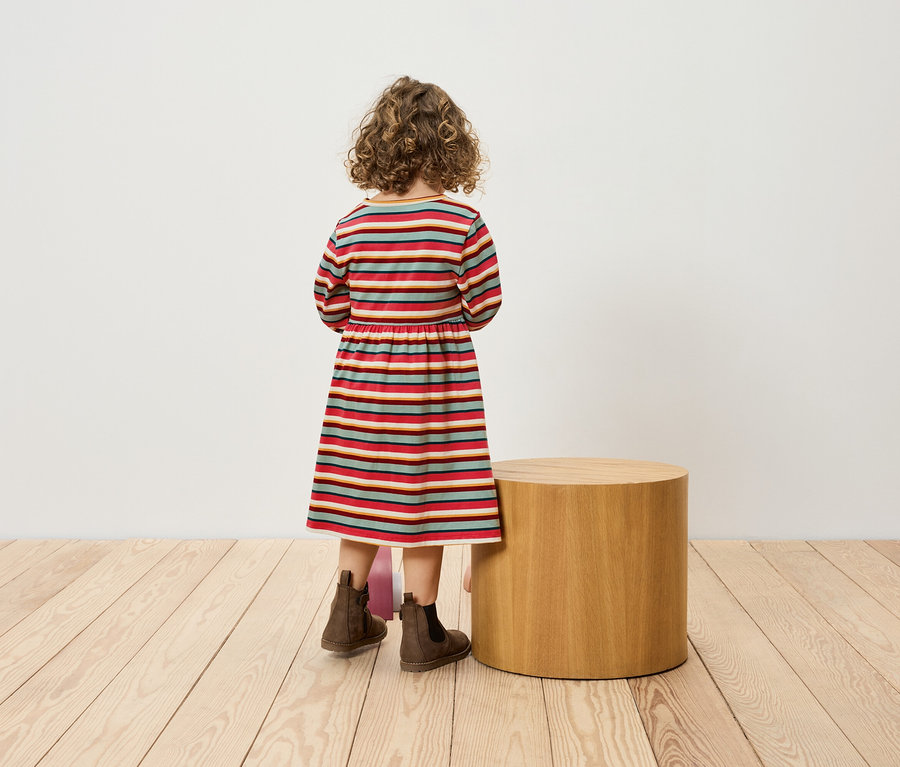 Une fille en robe rayée se tient dos à une petite table cylindrique et porte des bottes marron.