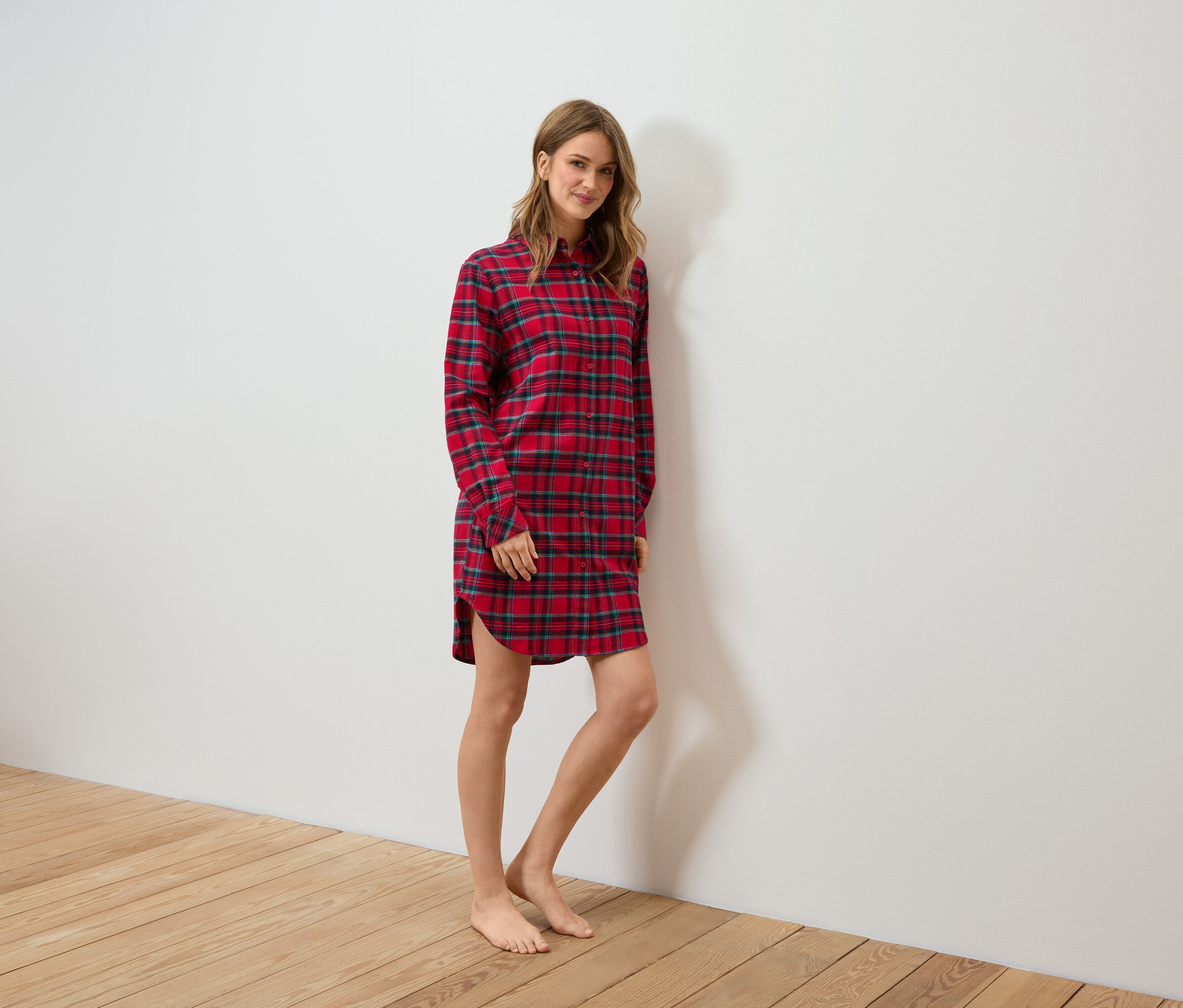 Une femme debout porte une chemise de nuit en flanelle à carreaux rouges.