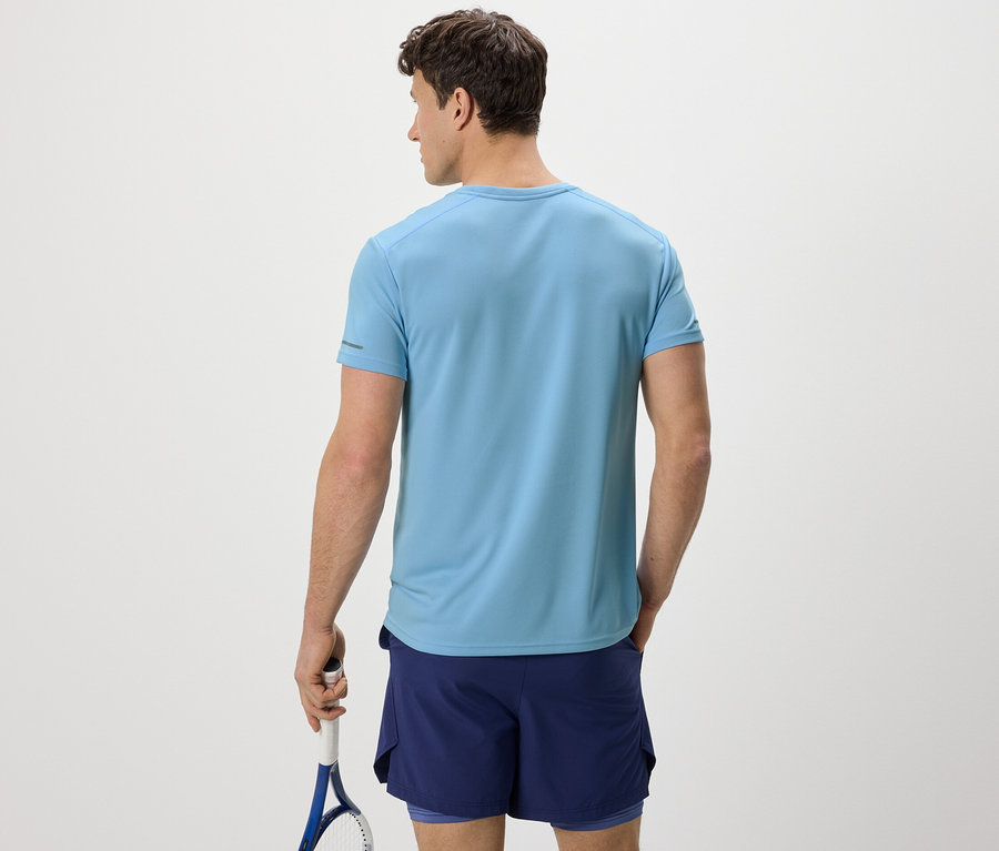 Un homme vu de dos portant un t-shirt fonctionnel bleu clair et tenant une raquette de tennis.
