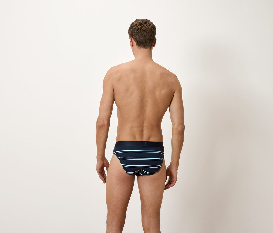 Un homme, vu de dos, porte un slip bleu avec des rayures horizontales.