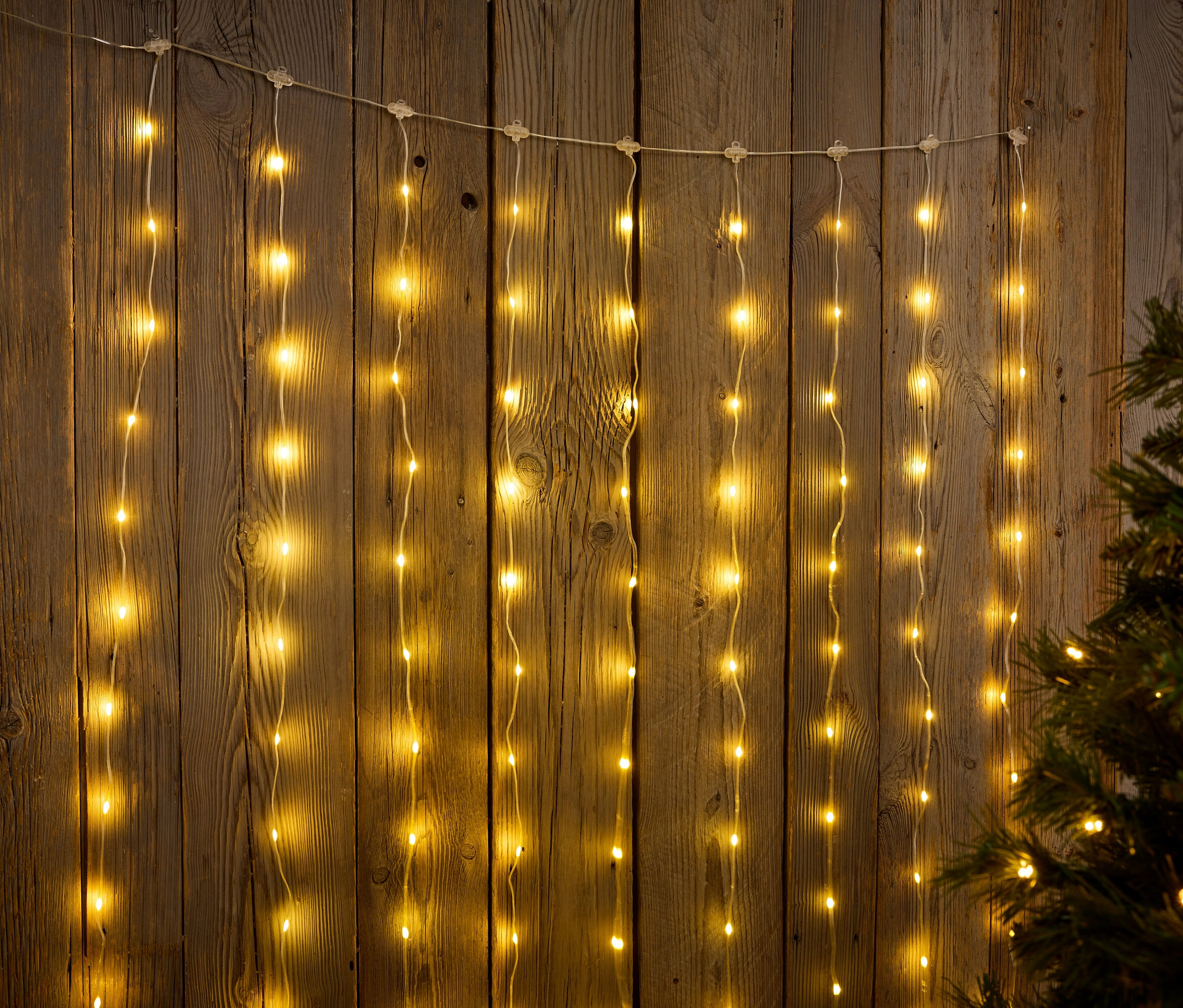 Guirlandes lumineuses suspendues sur un fond en bois à côté d'un arbre de Noël.