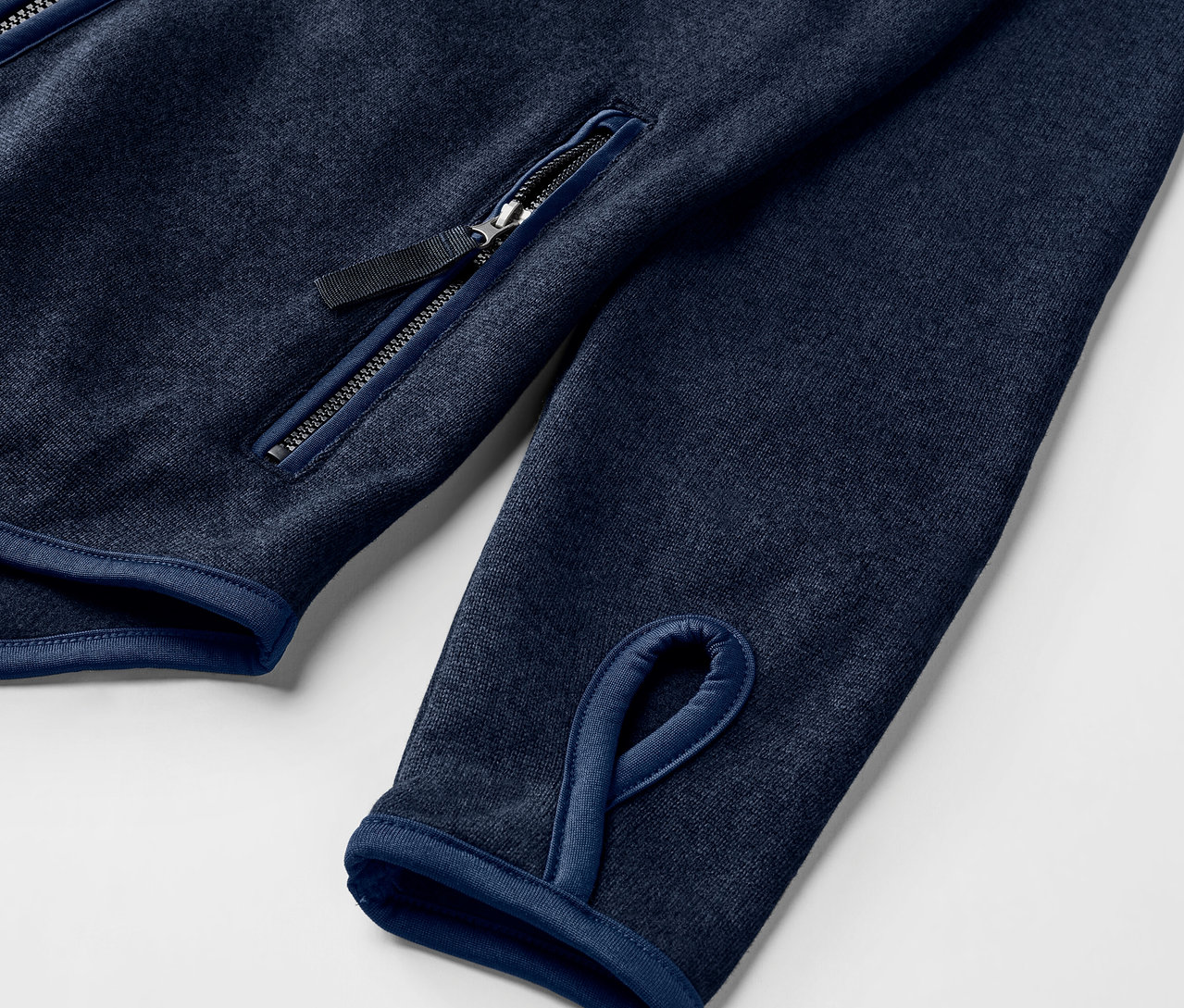 Détail d'une veste en maille polaire bleu marine avec trou pour le pouce et poche zippée.