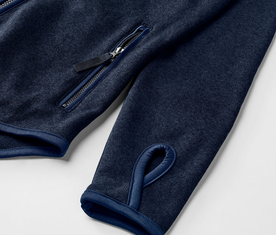 Détail d'une veste en maille polaire bleu marine avec trou pour le pouce et poche zippée.