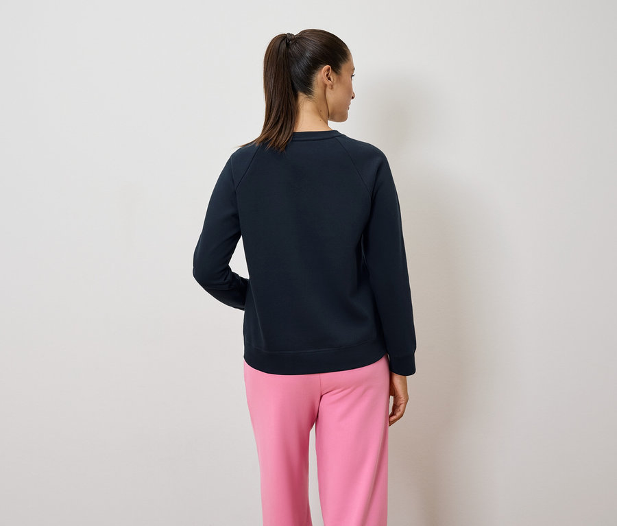Vue arrière d'une femme avec une queue de cheval portant un pull bleu marine et un pantalon rose.