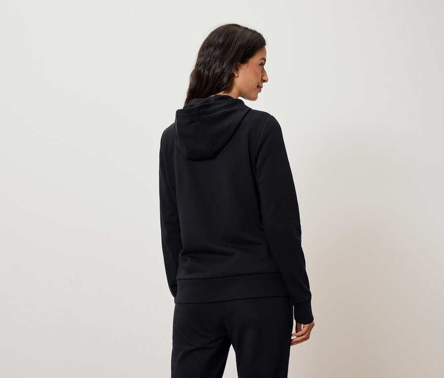 Une femme vue de dos porte un sweat à capuche noir et un pantalon noir.
