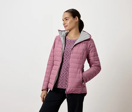 Femme portant une veste matelassée rose avec capuche et un pantalon bleu marine, regardant vers la gauche.