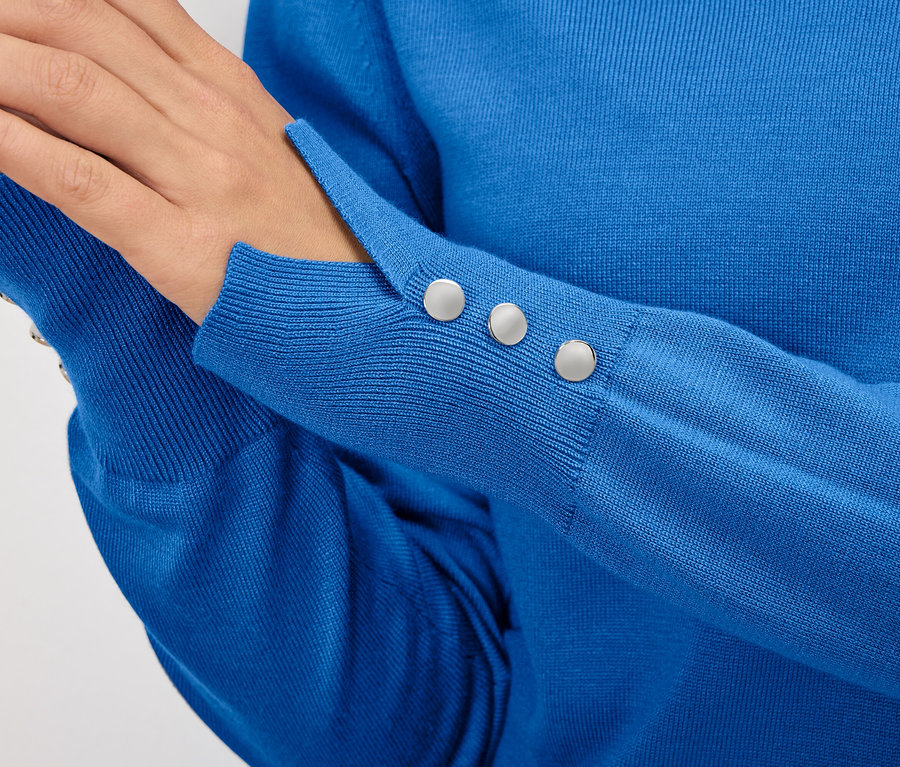 Détail d'un pull bleu pour femme avec des boutons sur la manche.