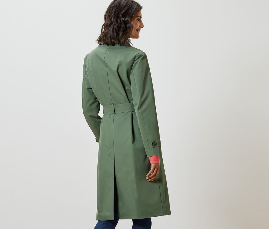 Une femme regarde par-dessus son épaule et porte un trench-coat vert clair.