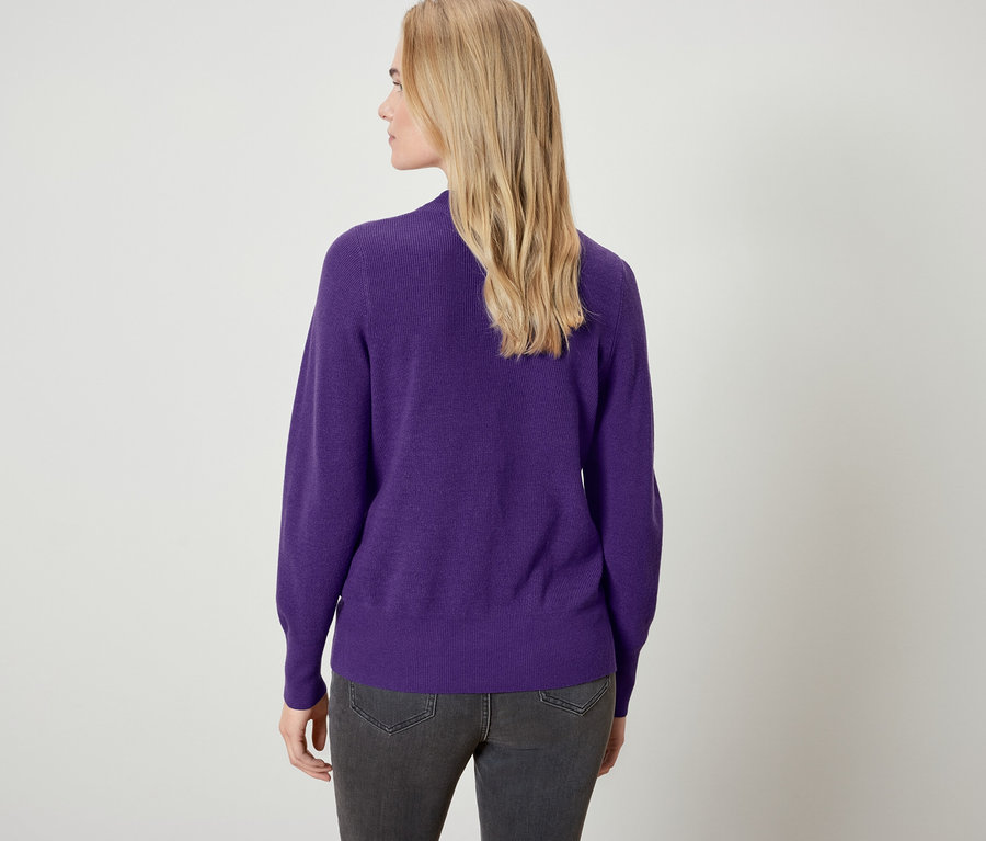Vue arrière d'une femme blonde portant un pull violet et un jean gris.