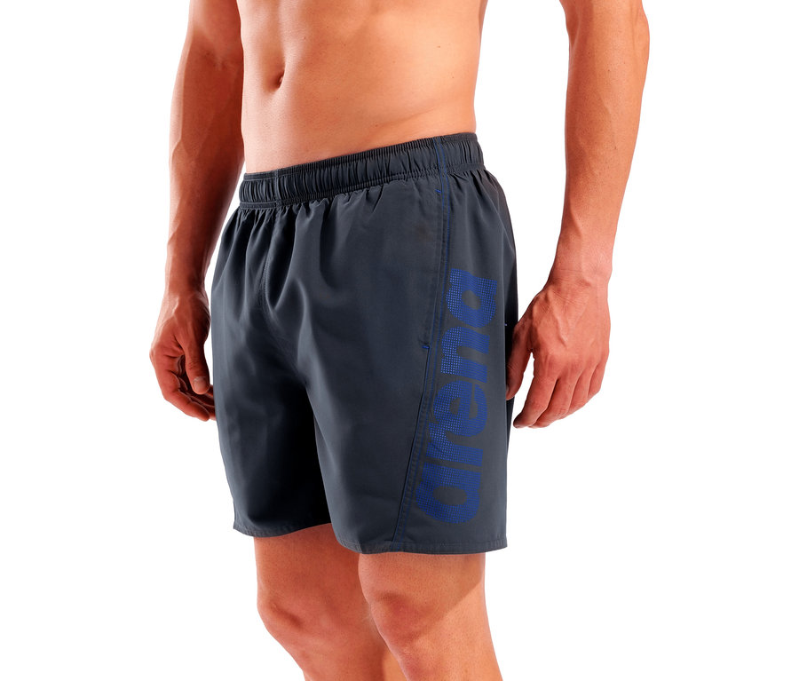 Homme portant un short de bain gris avec un lettrage bleu 'Arena' sur la jambe.