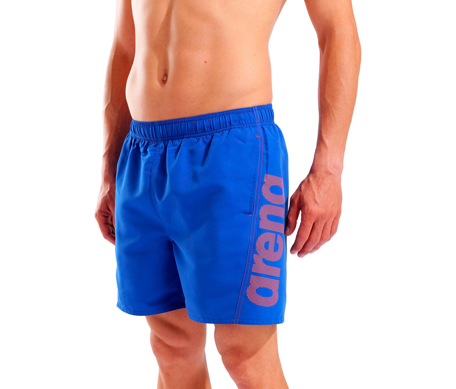 Un homme porte un short de bain bleu avec le logo Arena sur la jambe.