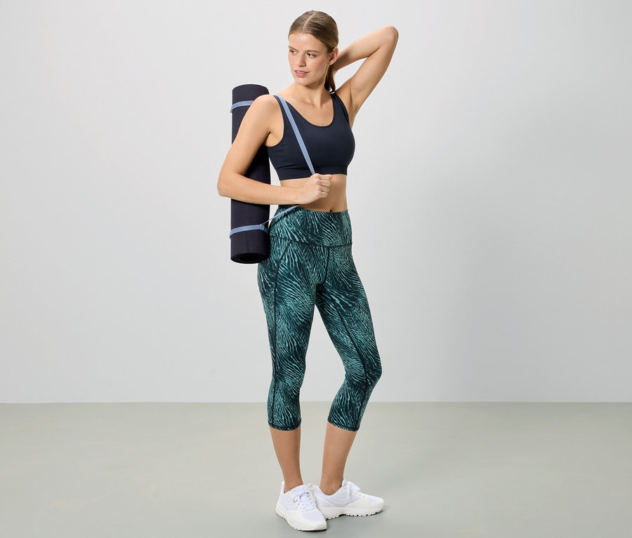 Femme en tenue de sport avec un tapis de yoga sur l'épaule.