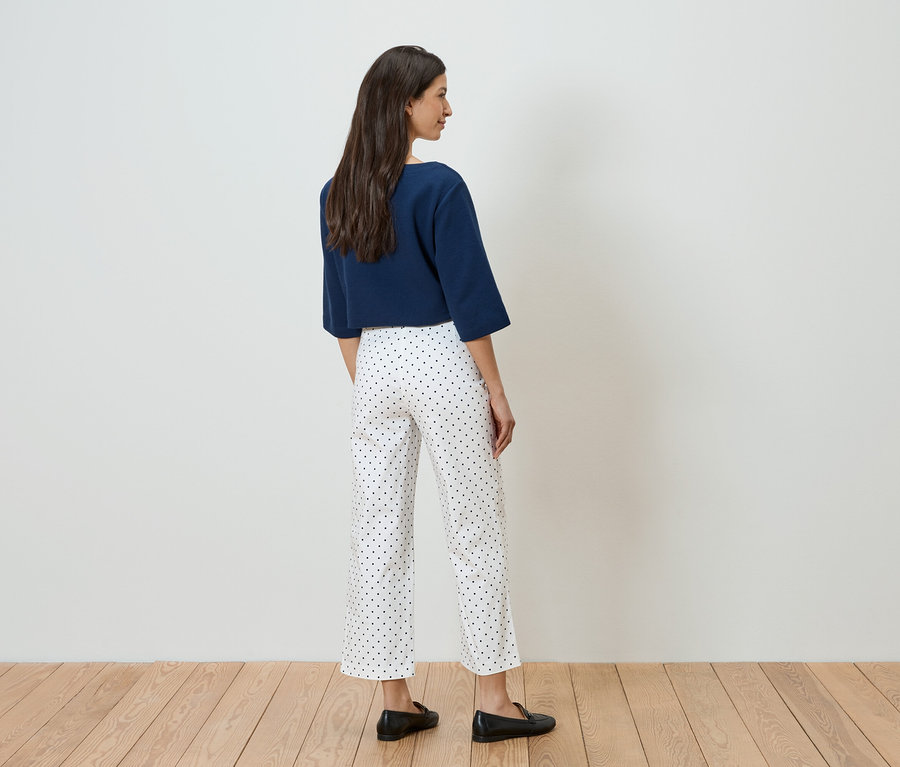 Une femme vue de dos portant un pull bleu marine et un pantalon blanc à pois bleus avec des chaussures noires.