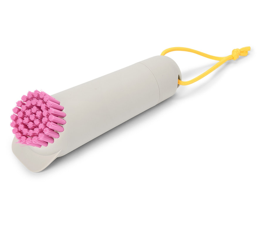 Une brosse grise avec des poils roses et une boucle jaune est posée sur un fond blanc.
