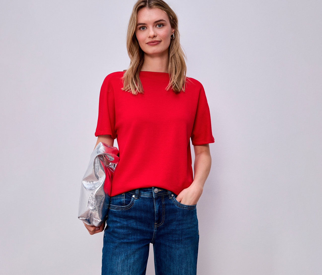 Femme portant une chemise à manches courtes Street One rouge et un jean, avec une veste argentée sur le bras.