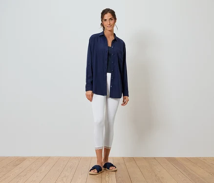 Femme debout devant un mur blanc portant une chemise bleue, un legging blanc et des pantoufles bleues.