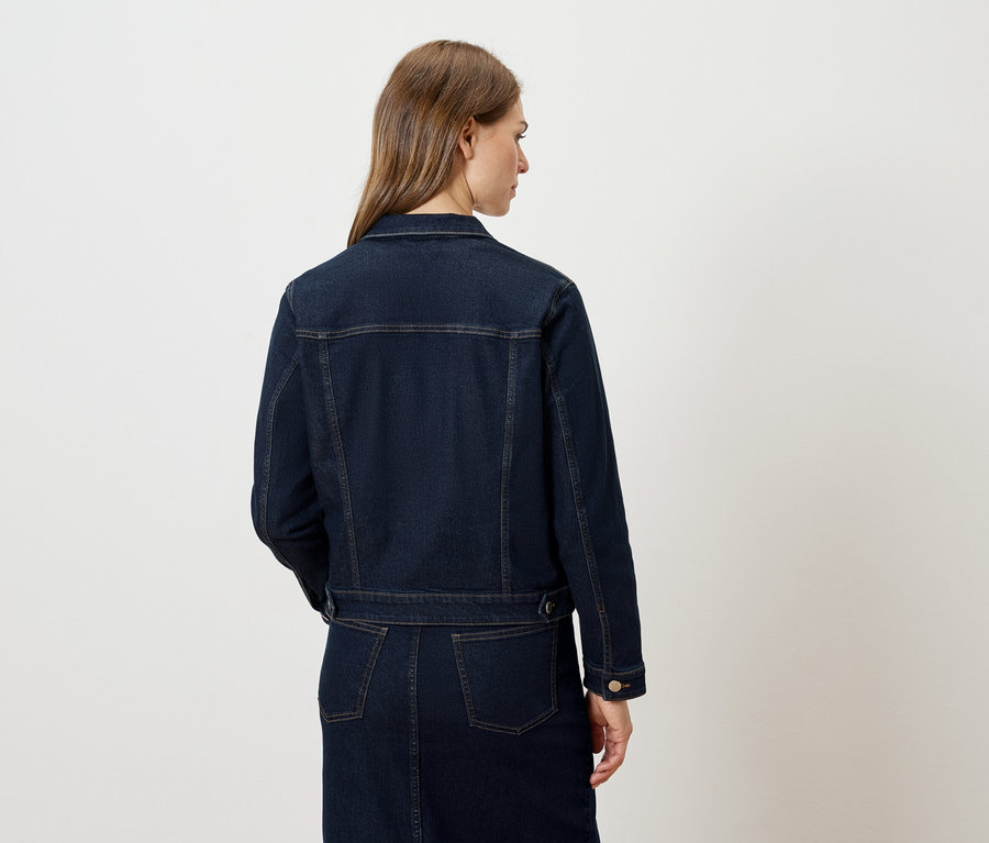 Vue arrière d'une femme portant une veste et une jupe en jean bleu foncé.
