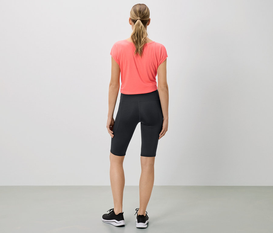 Femme vue de dos portant un t-shirt corail, un short de cycliste noir et des baskets.