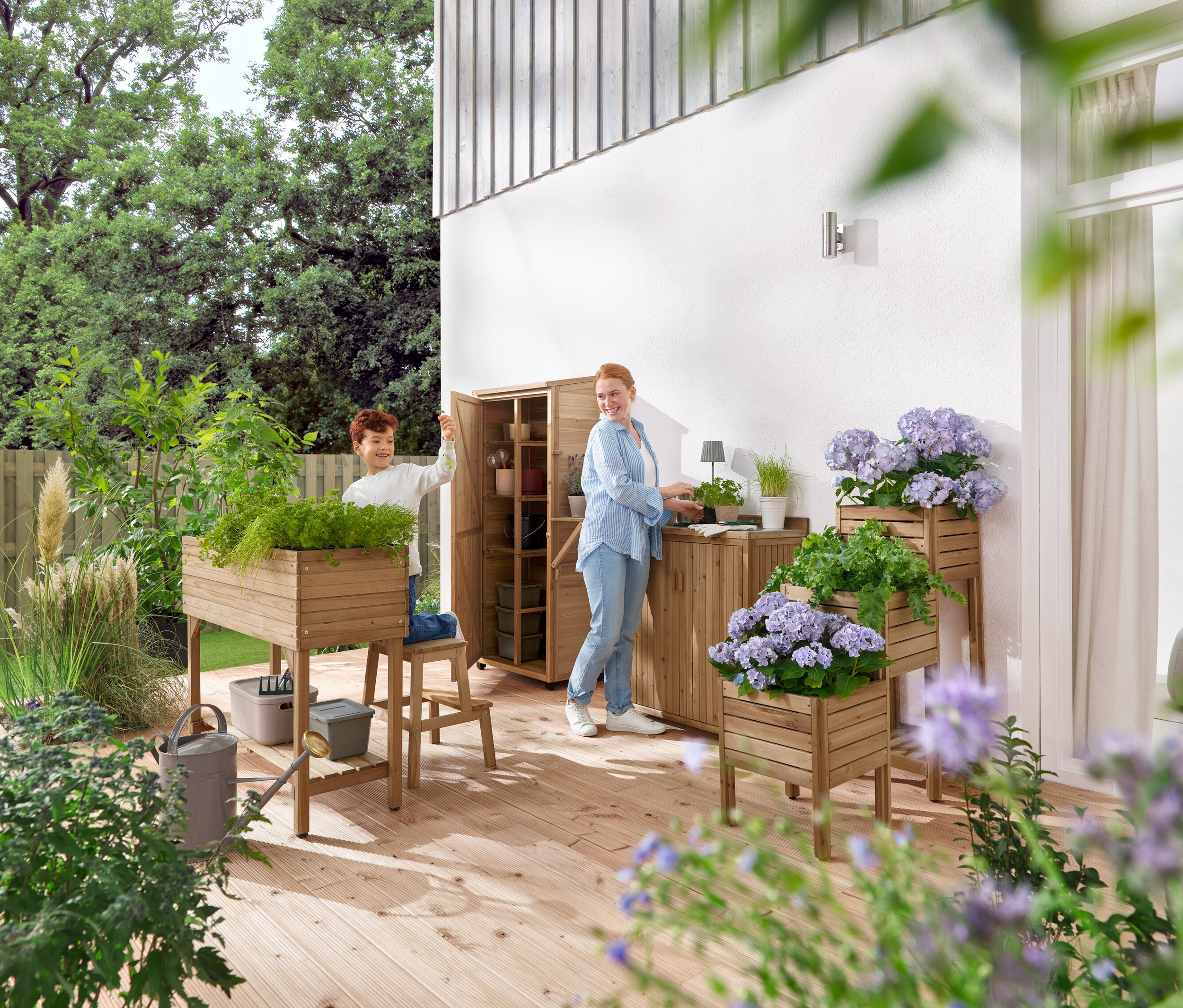 Un garçon et une femme manipulent du mobilier de jardin et des plantes sur une terrasse en bois.