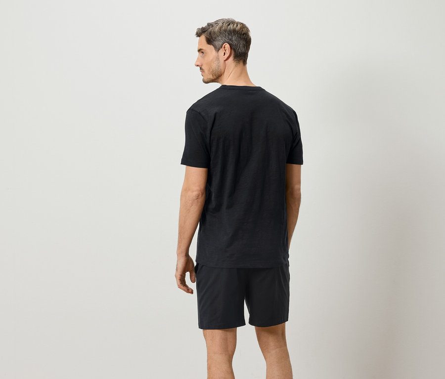 Homme vu de dos, portant un t-shirt noir et un short sur un fond blanc.