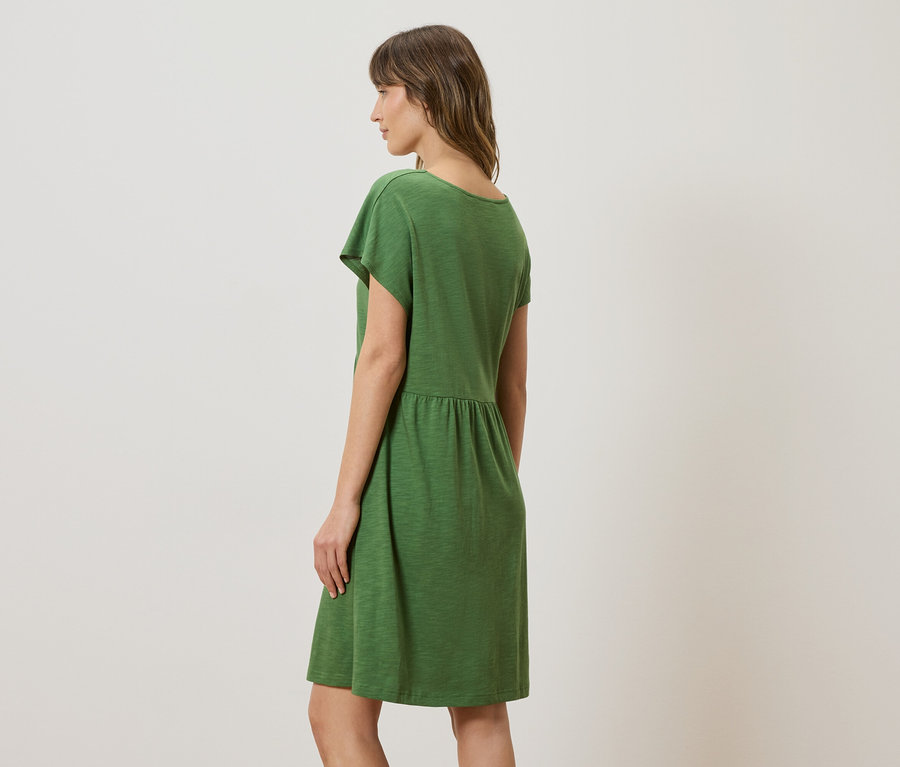 Femme debout de profil portant une robe verte.