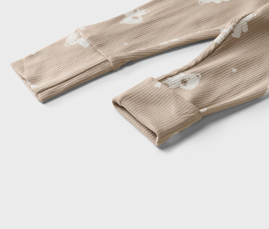 Gros plan sur un pantalon de bébé beige côtelé avec motif ours et ourlets retroussés.