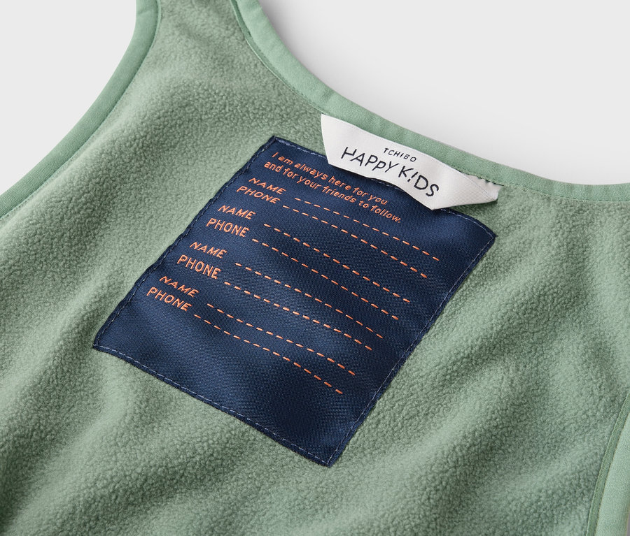 Vue intérieure d'un gilet pour enfant vert clair avec une étiquette indiquant « HAPPY KIDS » et un espace pour saisir les noms et numéros de téléphone.