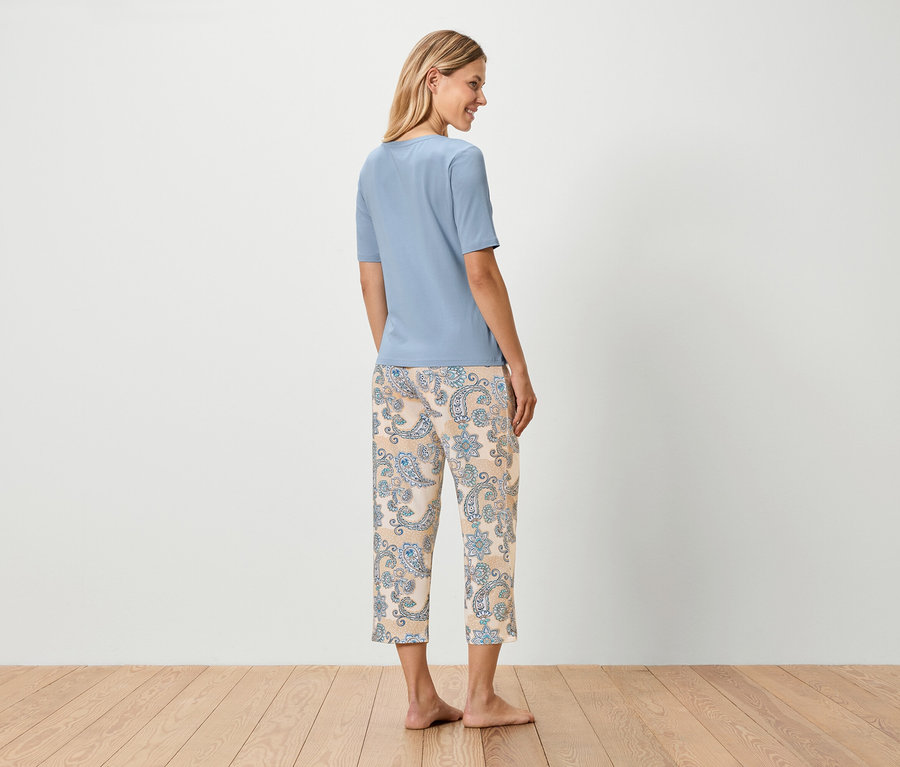 Femme debout, dos à la caméra, portant un t-shirt bleu et un pantalon beige avec un motif cachemire bleu.