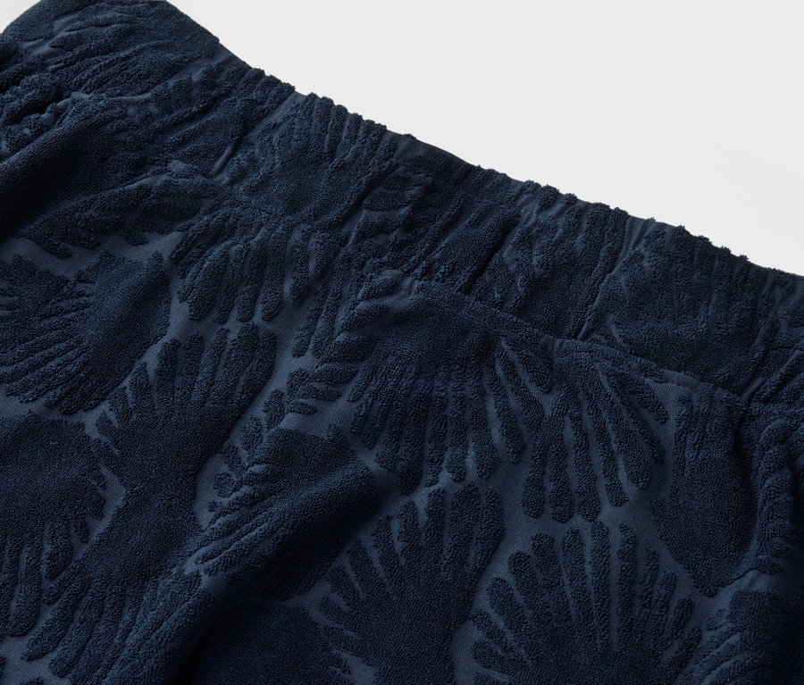 Gros plan sur le haut d'un pantalon texturé bleu marine avec une ceinture élastique et un motif de palmiers.