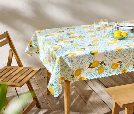Table à manger avec une nappe à motif citron, de la vaisselle et des verres, à côté d'une chaise en bois.