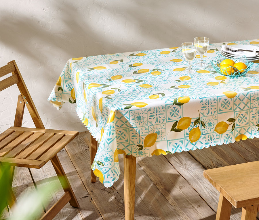 Table à manger avec une nappe à motif citron, de la vaisselle et des verres, à côté d'une chaise en bois.