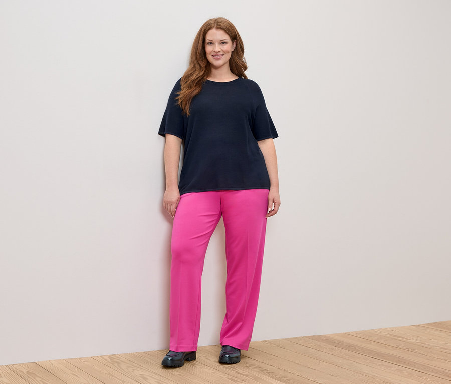 Femme aux longs cheveux roux portant un t-shirt bleu marine et un pantalon rose.