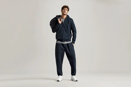 Homme portant un sweat à capuche bleu marine et un pantalon de jogging bleu marine, avec un sac sur l'épaule.