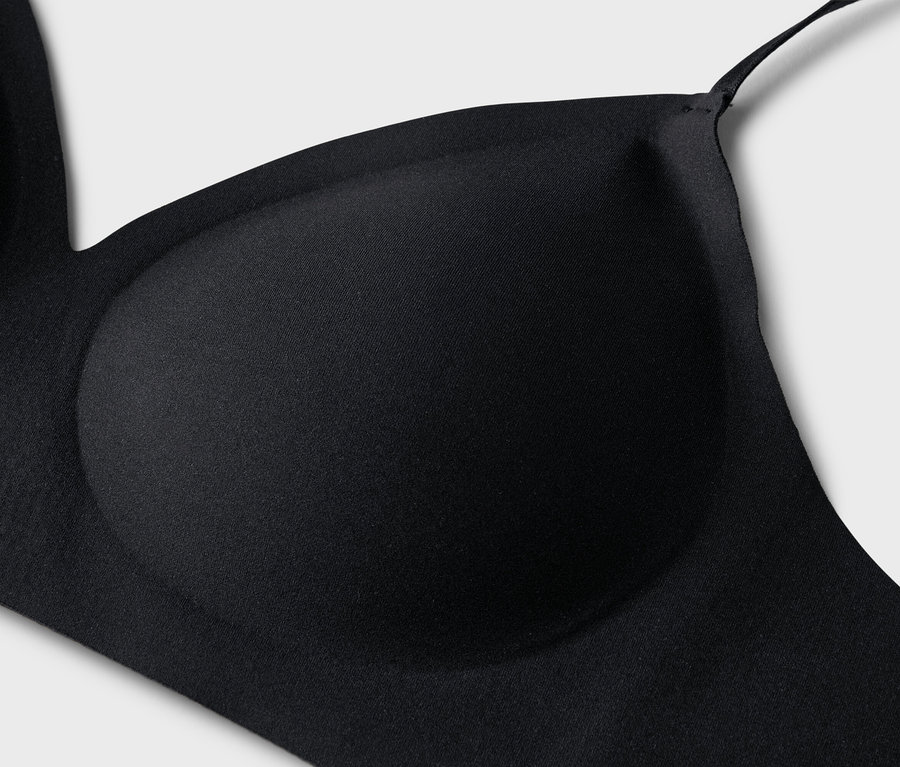Gros plan d'un soutien-gorge noir avec des bonnets moulés et de fines bretelles sur un fond gris clair.