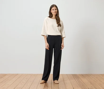 Femme portant un chemisier crème à manches trois-quarts et un pantalon noir à plis, avec des chaussures beiges.