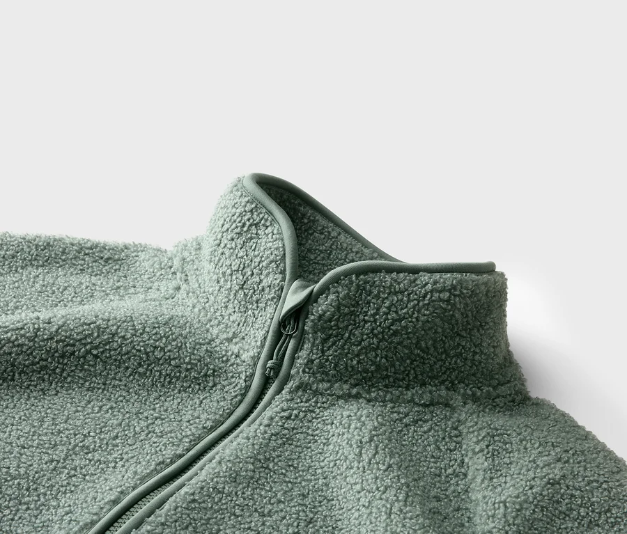 Gros plan d'une veste en polaire vert clair avec fermeture éclair et col montant sur fond blanc.