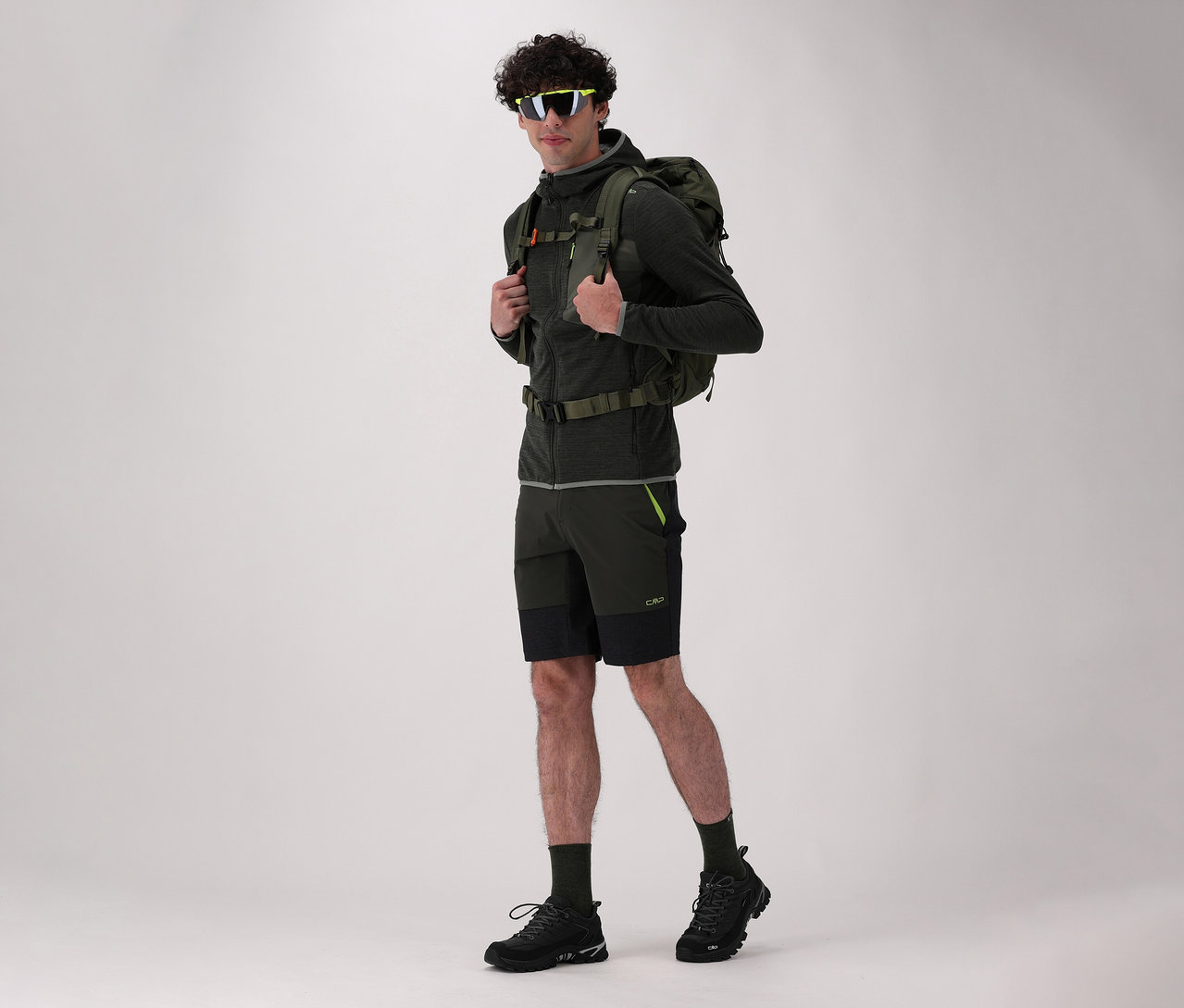 Un homme avec un sac à dos et des chaussures de trekking CMP RIGEL LOW 2.0 WP noires pose sur un fond clair.