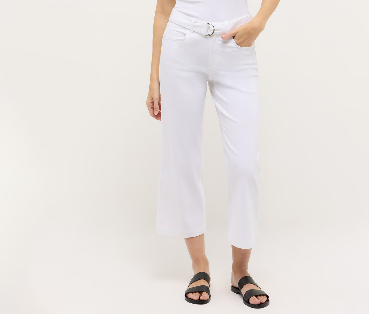 Une personne porte un jean Angels Denim « Linn City » court, blanc, avec une ceinture argentée et des sandales noires.